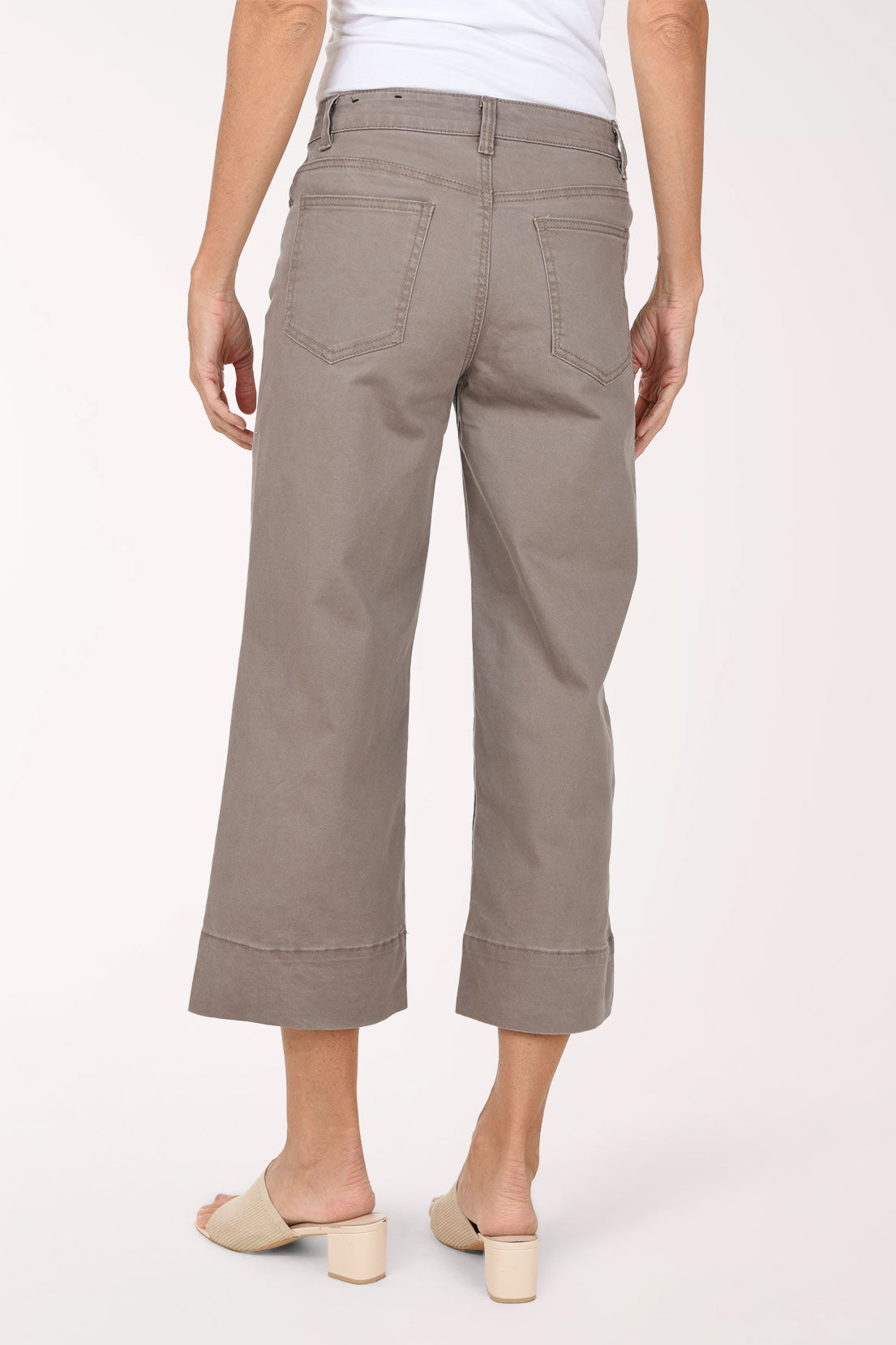 A model wearing a pair of taupe cropped wide-leg jeans with rolled hems, paired with beige slide sandals, against a plain light background.