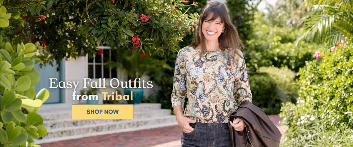 Model wearing a colorful floral print Tribal top with dark denim jeans, holding a brown jacket outdoors. Shop easy fall outfits from Tribal at Anthony's.