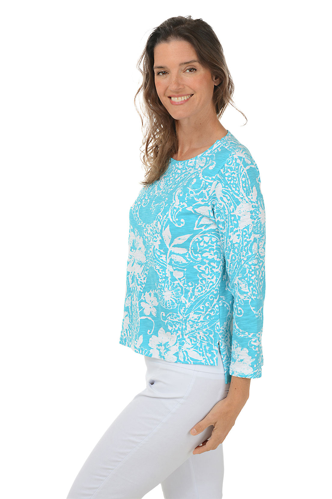 A woman wearing a blue and white paisley scroll 3/4 sleeve knit top with a scoop neckline and high-low hemline. Side shot.