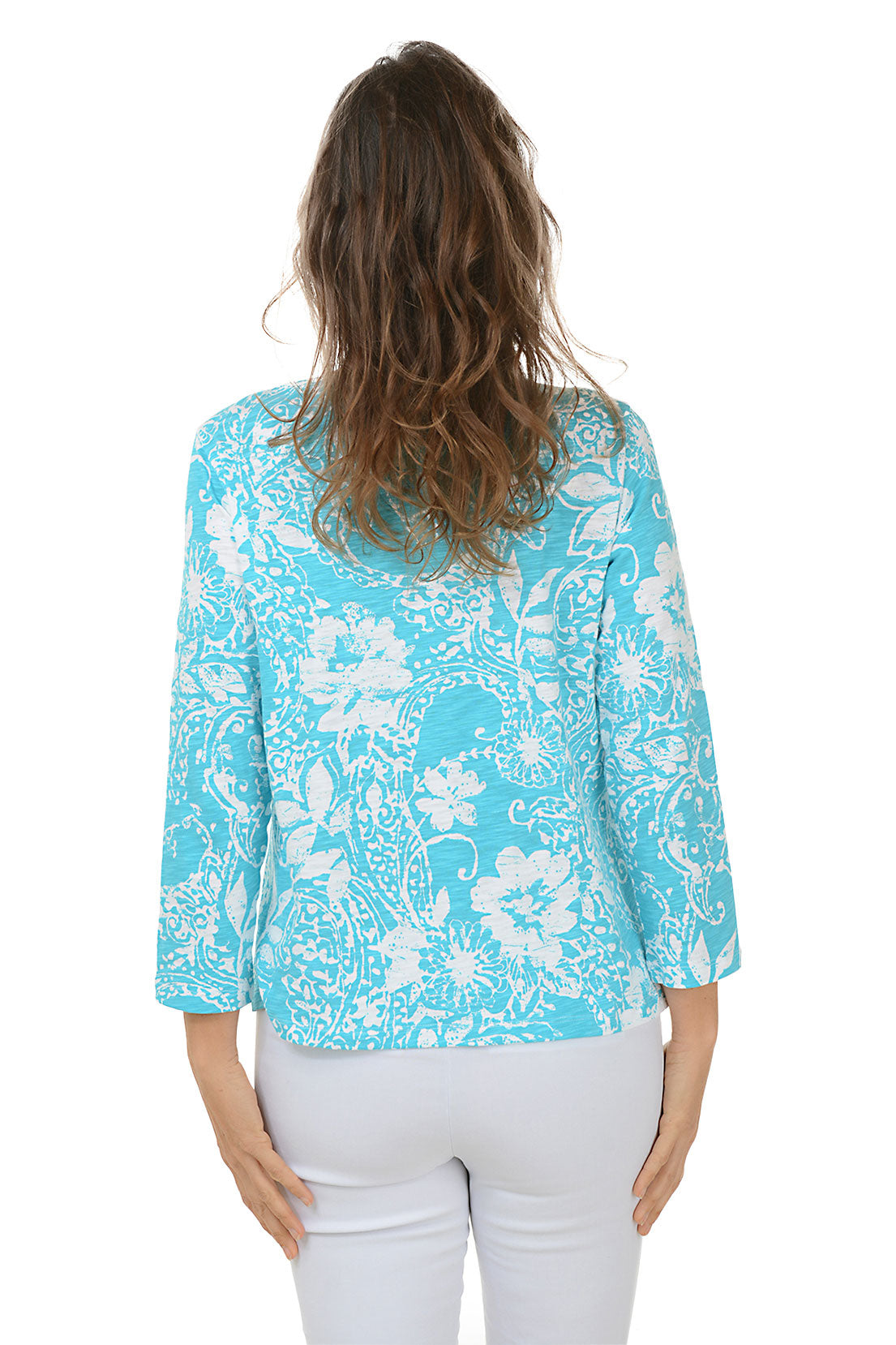 A woman wearing a blue and white paisley scroll 3/4 sleeve knit top with a scoop neckline and high-low hemline. Back shot.