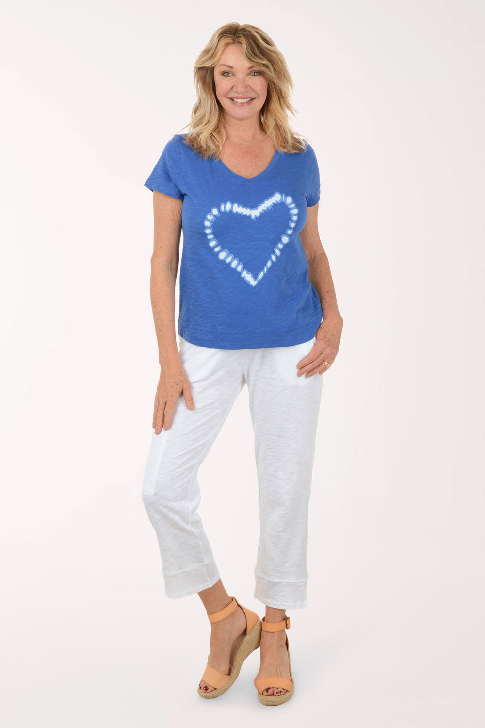 Woman wearing a blue t-shirt with a white heart design and white pants on a white background