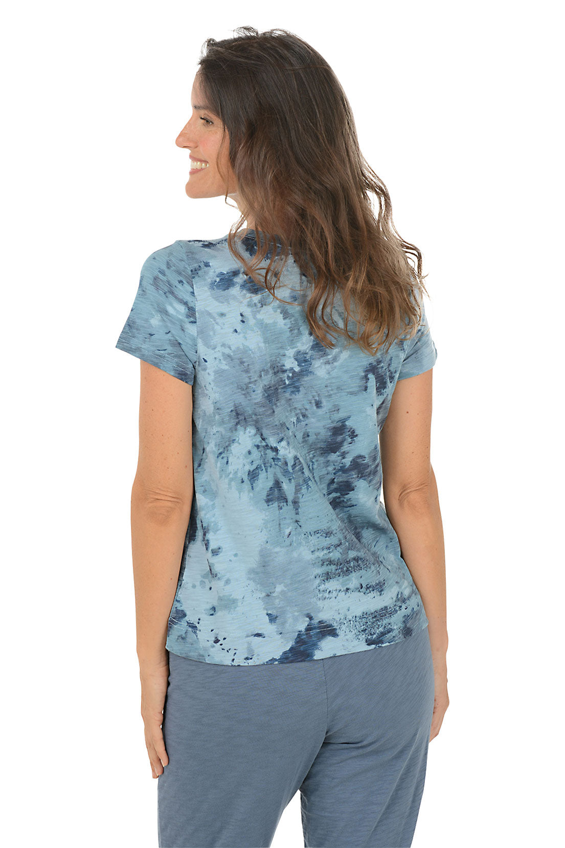 Woman wearing a blue tie dye top and denim pants on a white background. Back shot.