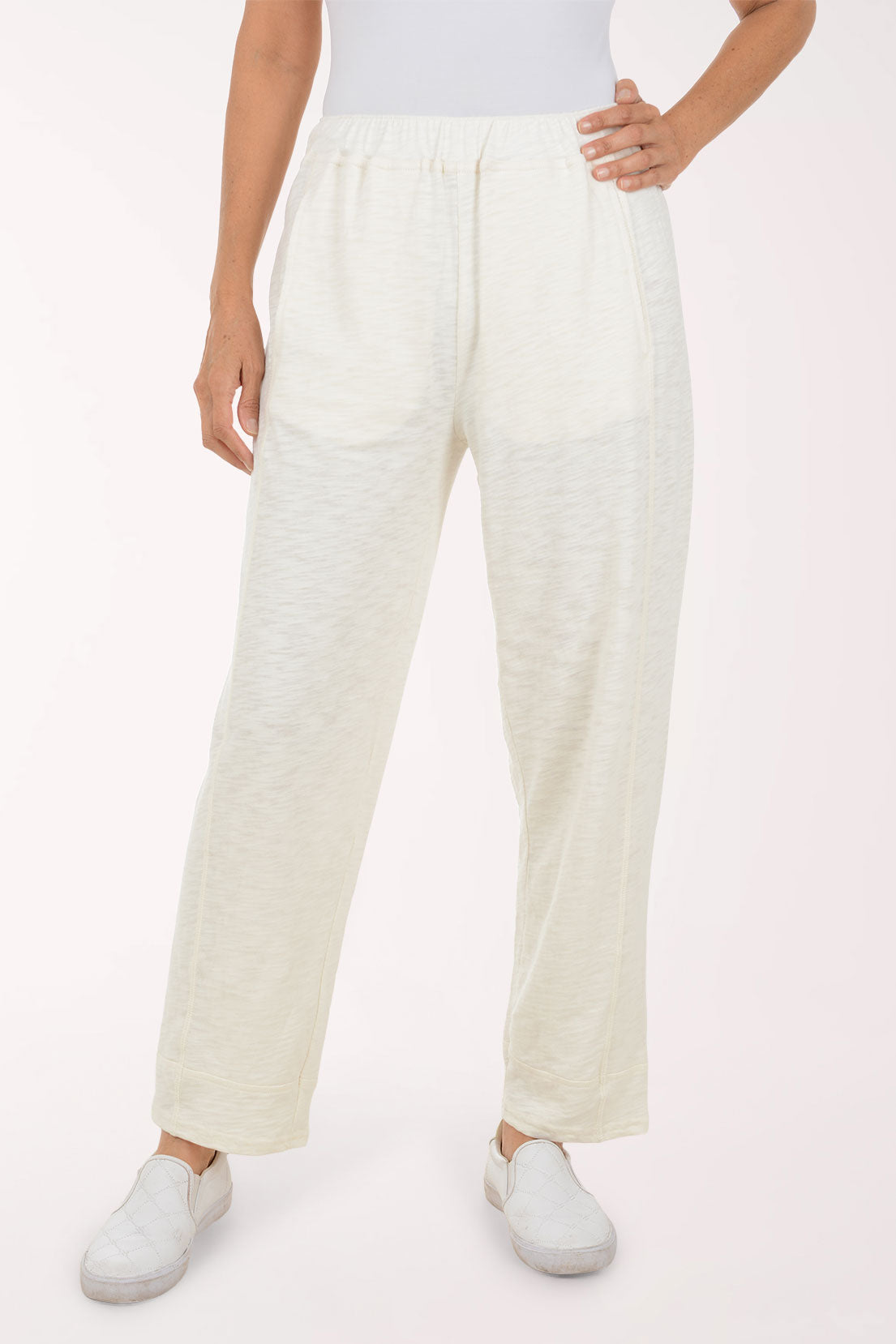 A person wearing loose, high-waisted off-white linen pants with side pockets and white slip-on shoes, shown against a plain light background.