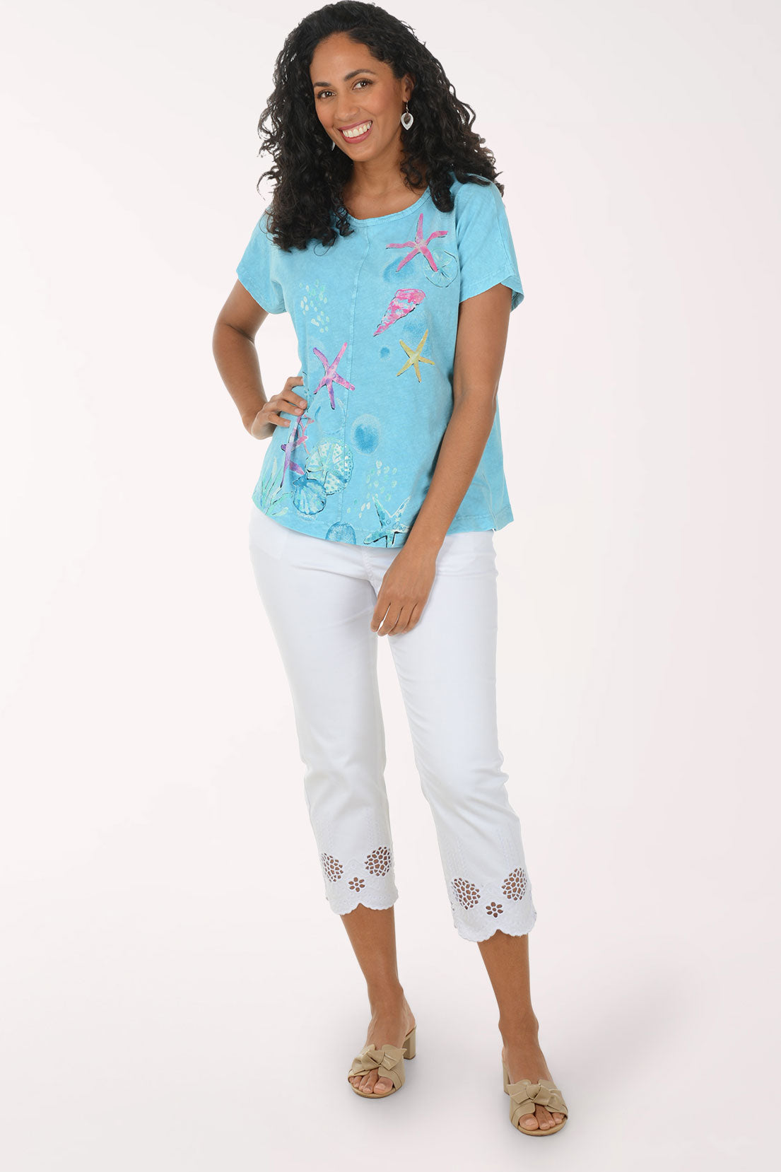 Woman wearing a blue embroidered top and white pants on a white background