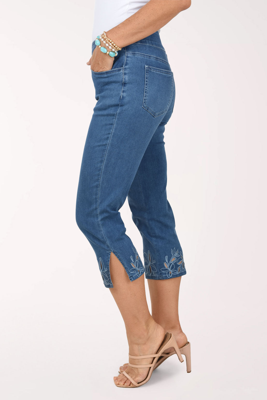 A side view of the denim capri pants showing the side slit and floral cut-out detail at the hem.