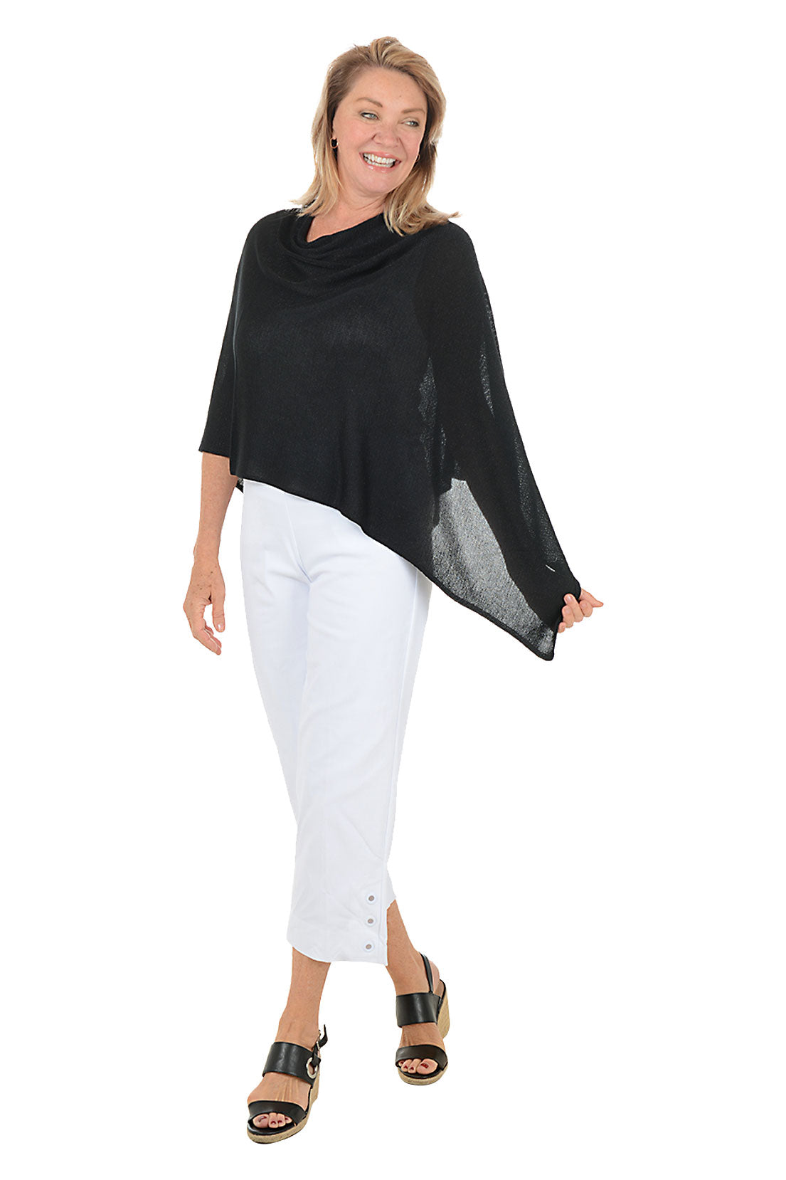 Woman wearing a black poncho and white pants on a white background