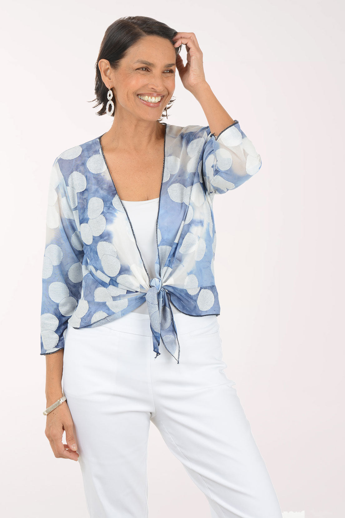 Woman wearing a blue and white patterned shrug over a white top and pants on a white background
