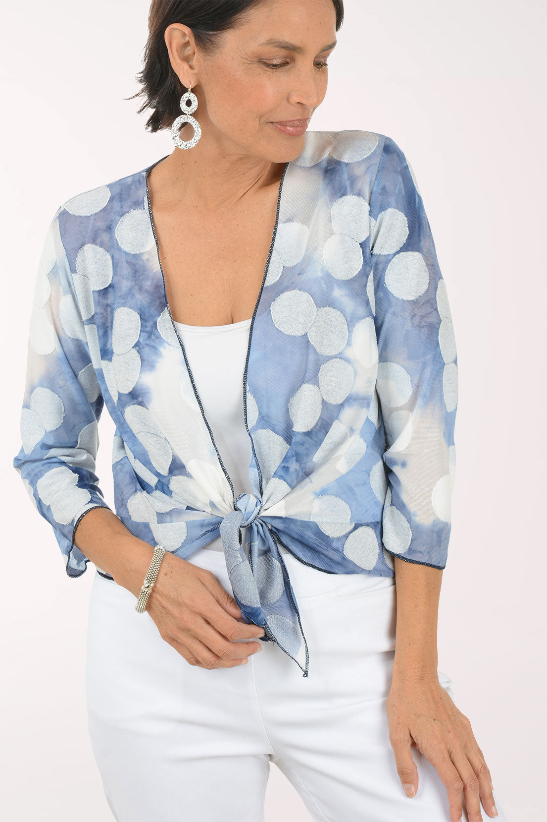 Woman wearing a blue and white patterned shrug over a white top and pants on a white background