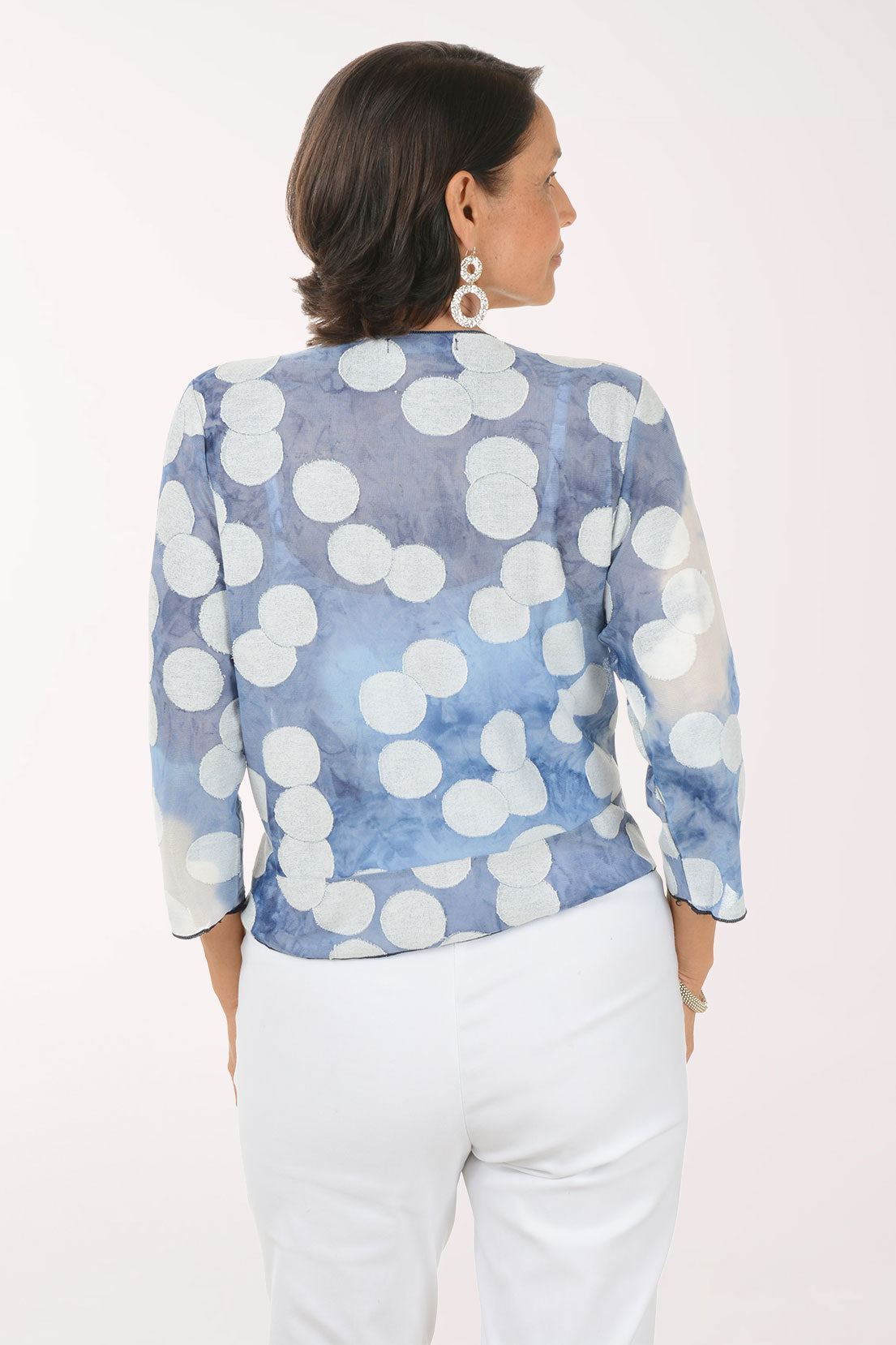 Woman wearing a blue and white patterned shrug over a white top and pants on a white background