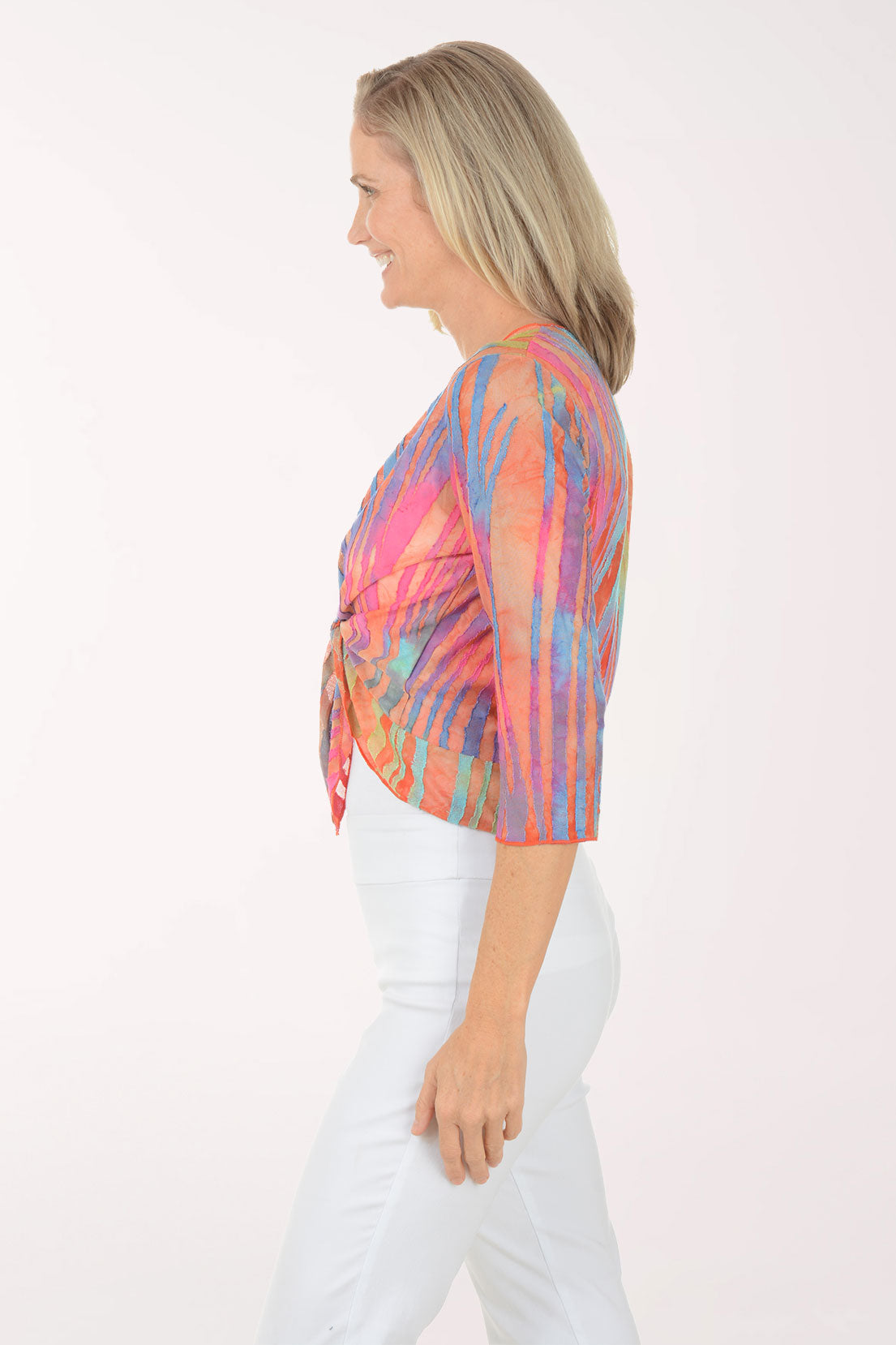 Woman wearing a multi colored patterned shrug over a white top and pants on a white background