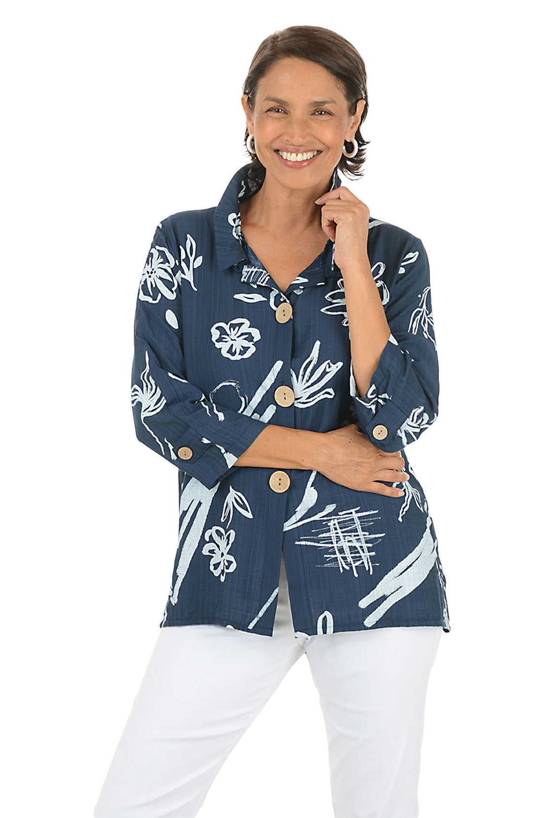 Woman wearing a navy blue floral patterned blouse with white pants on a white background.