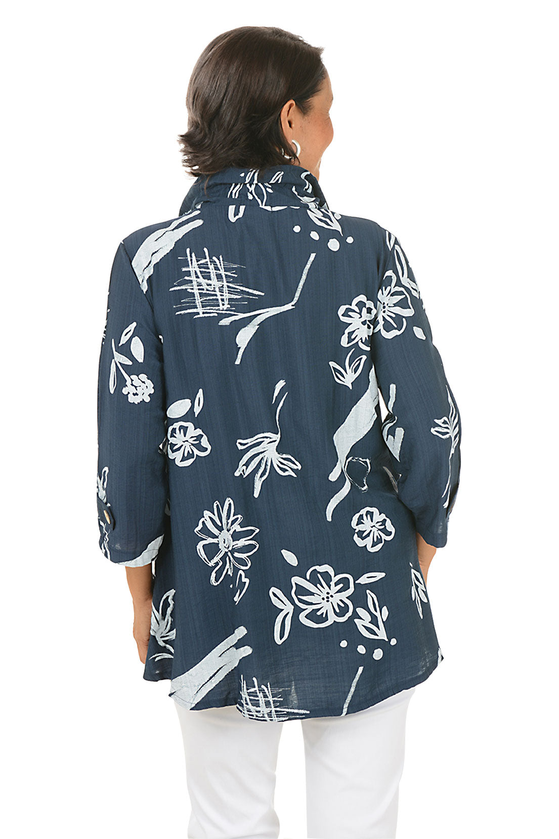 Woman wearing a navy blue floral patterned blouse with white pants on a white background. Back shot.