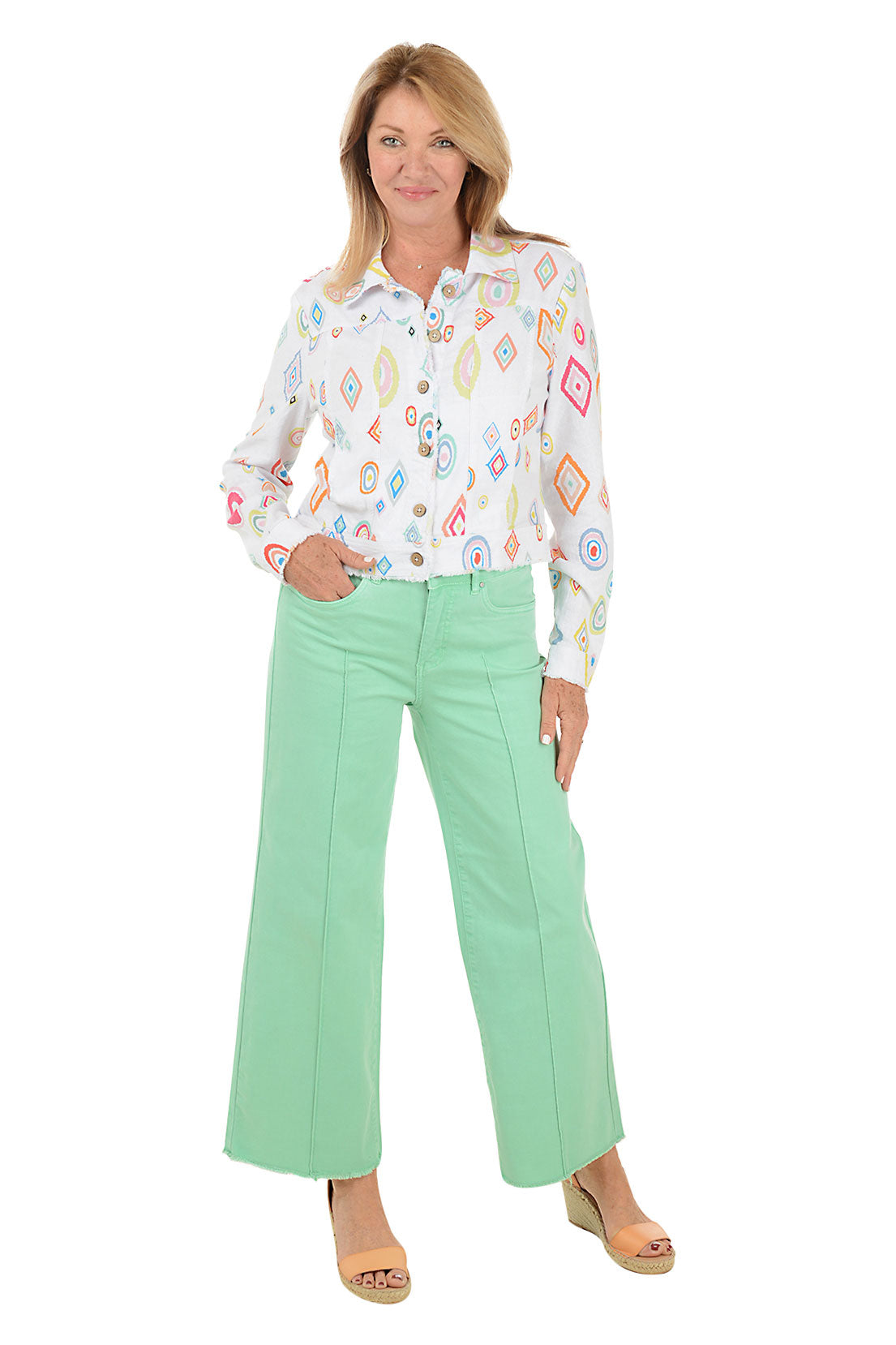 A full length shot of a model wearing a pair of mint green denim ankle pants with a pintuck front seam, wide leg, and frayed hemline. The pants have a high waist with belt loops and a button-and-zip fly.