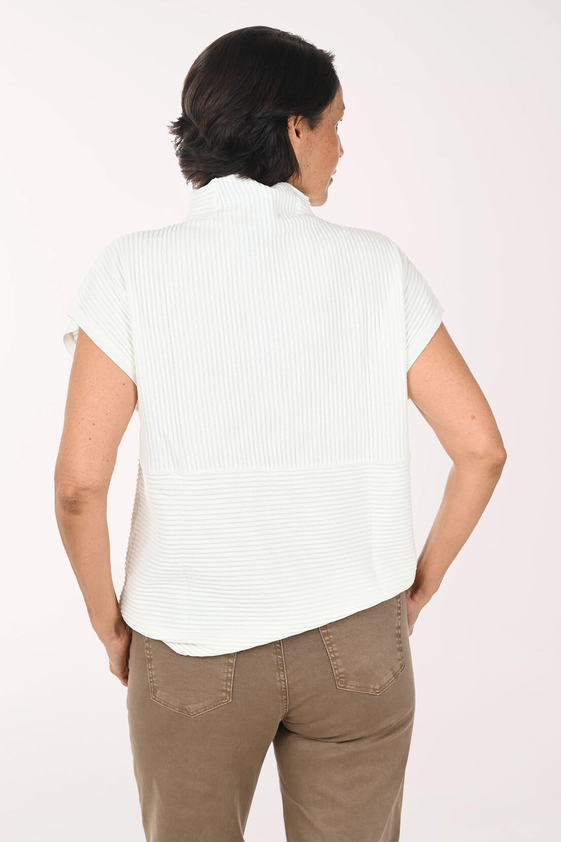 A woman viewed from the back wearing a white short-sleeve ribbed mock-neck top and brown pants against a plain light background.