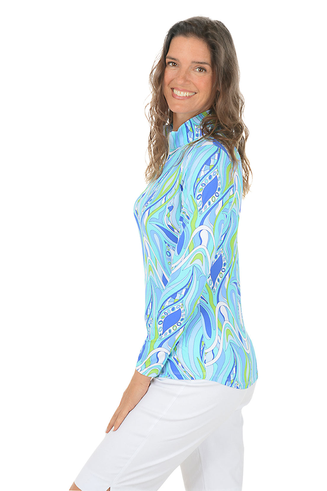 Woman wearing a blue and green patterned shirt with white pants on a white background. Side shot.