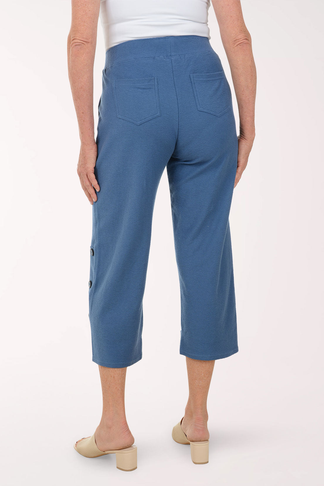 Blue pants with button details worn by a person on a white background