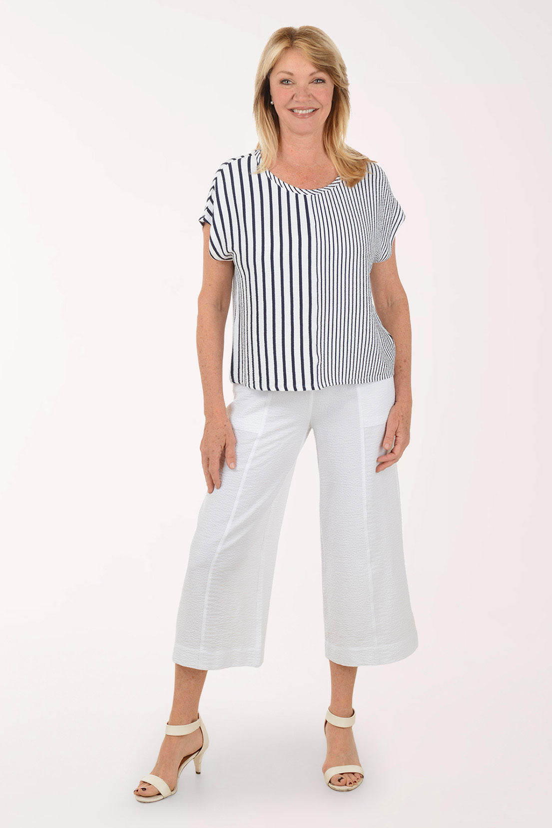 Woman wearing a black and white striped top and white pants on a white background
