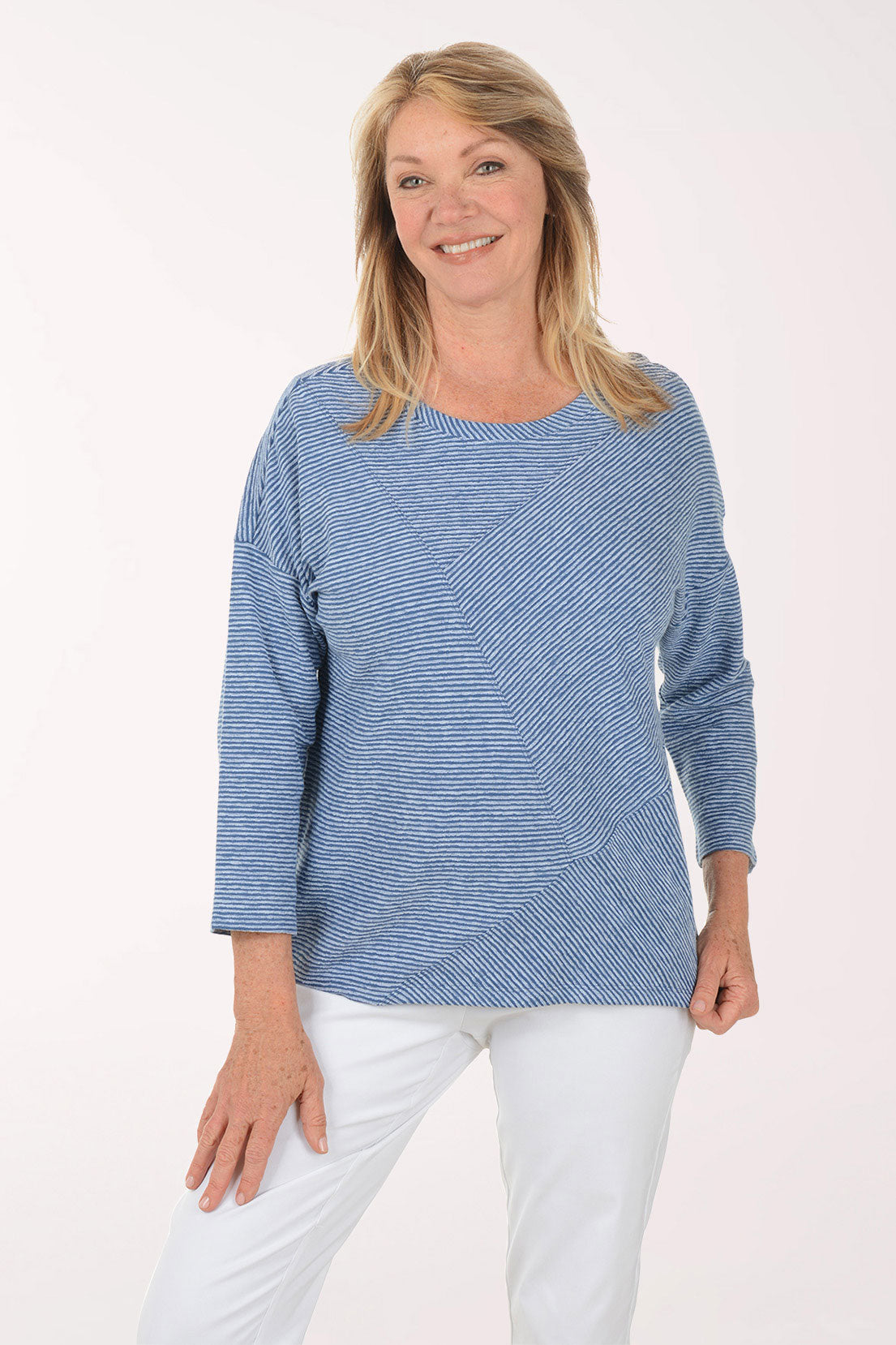 Woman wearing a blue striped sweater and white pants on a white background