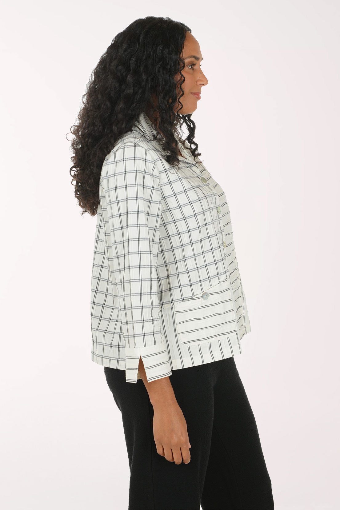 A woman shown in side profile wearing a light green and white plaid cropped jacket with black pants, photographed against a plain white studio background.