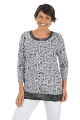 A front shot of a model wearing a black and white geometric patterned tunic with a pleated back detail and a scoop neckline.