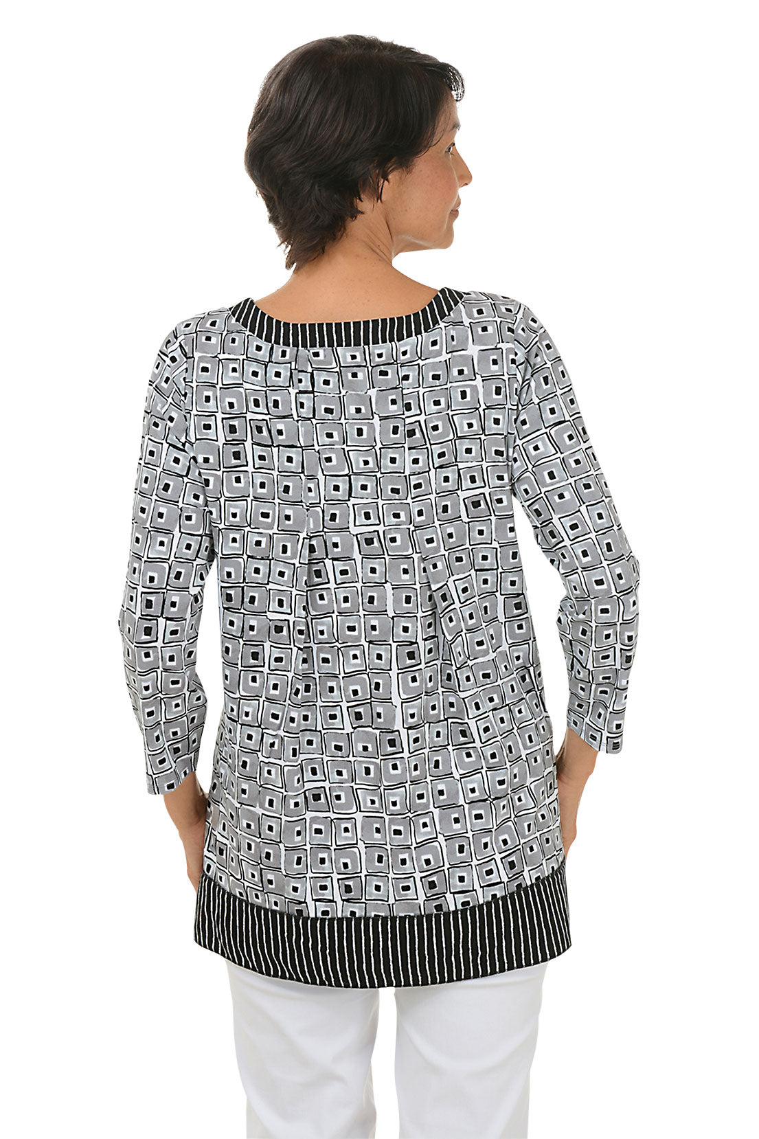 A back shot of a model wearing a black and white geometric patterned tunic with a pleated back detail and a scoop neckline.