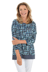 A front shot of a model wearing a blue and white geometric patterned tunic with a scoop neckline and pleated detail on the back.