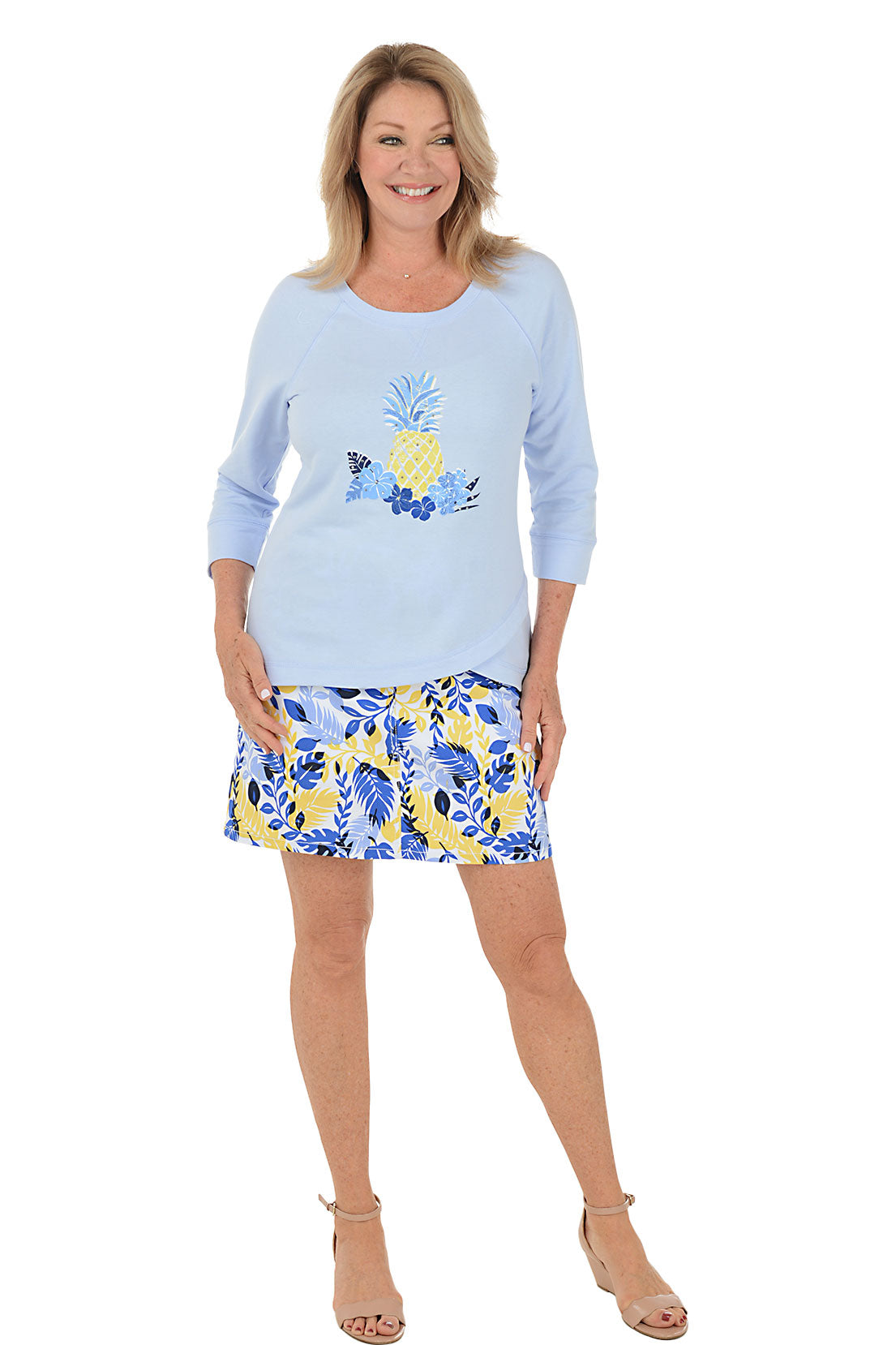 A full length shot of a model wearing a blue and yellow floral skort with a pair of tan ankle strap heels.