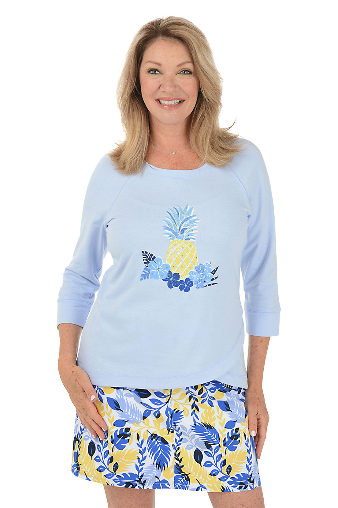 A front shot of a model wearing a light blue long-sleeve top with a pineapple design and a multicolored skirt with a floral pattern.