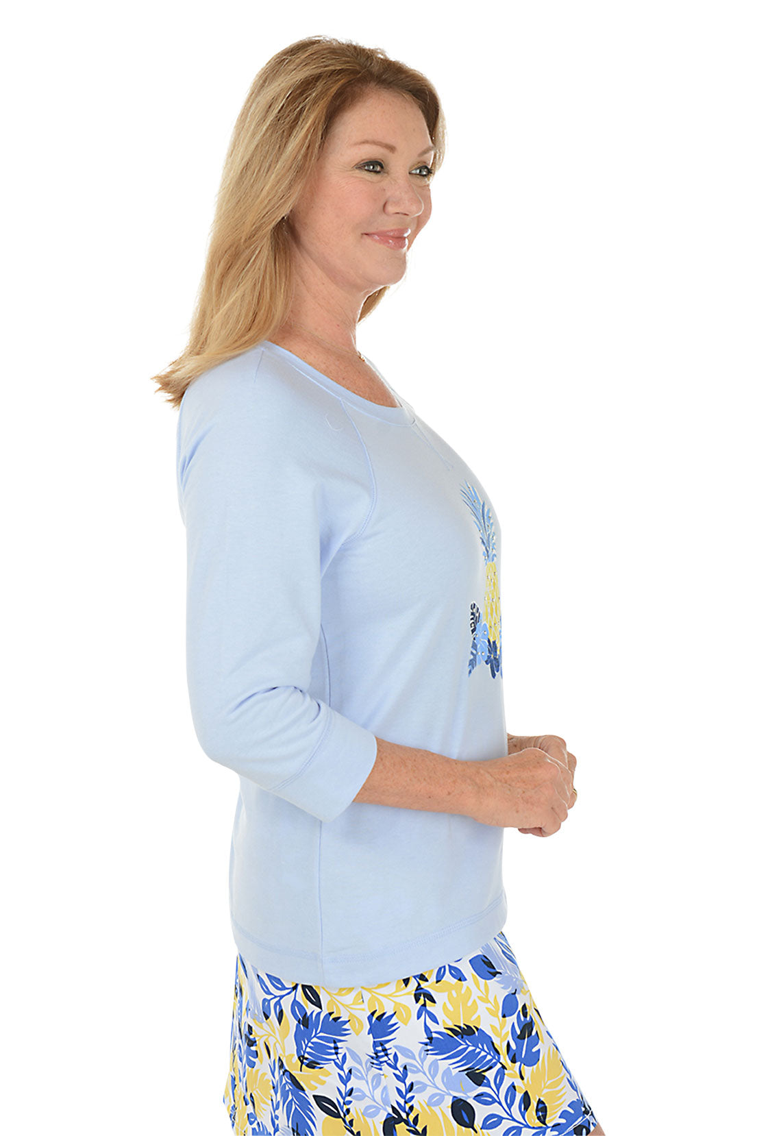A side shot of a model wearing a light blue long-sleeve top with a pineapple design and a multicolored skirt with a floral pattern.