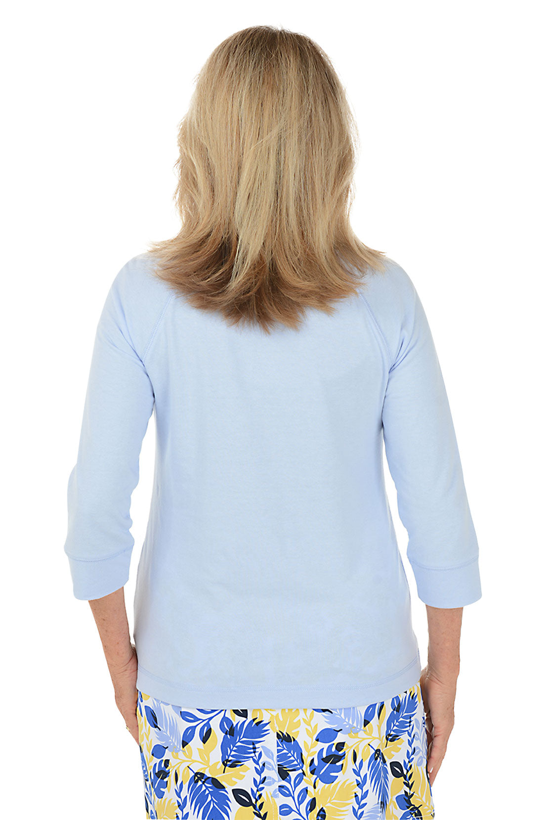 A back shot of a model wearing a light blue long-sleeve top with a pineapple design and a multicolored skirt with a floral pattern.