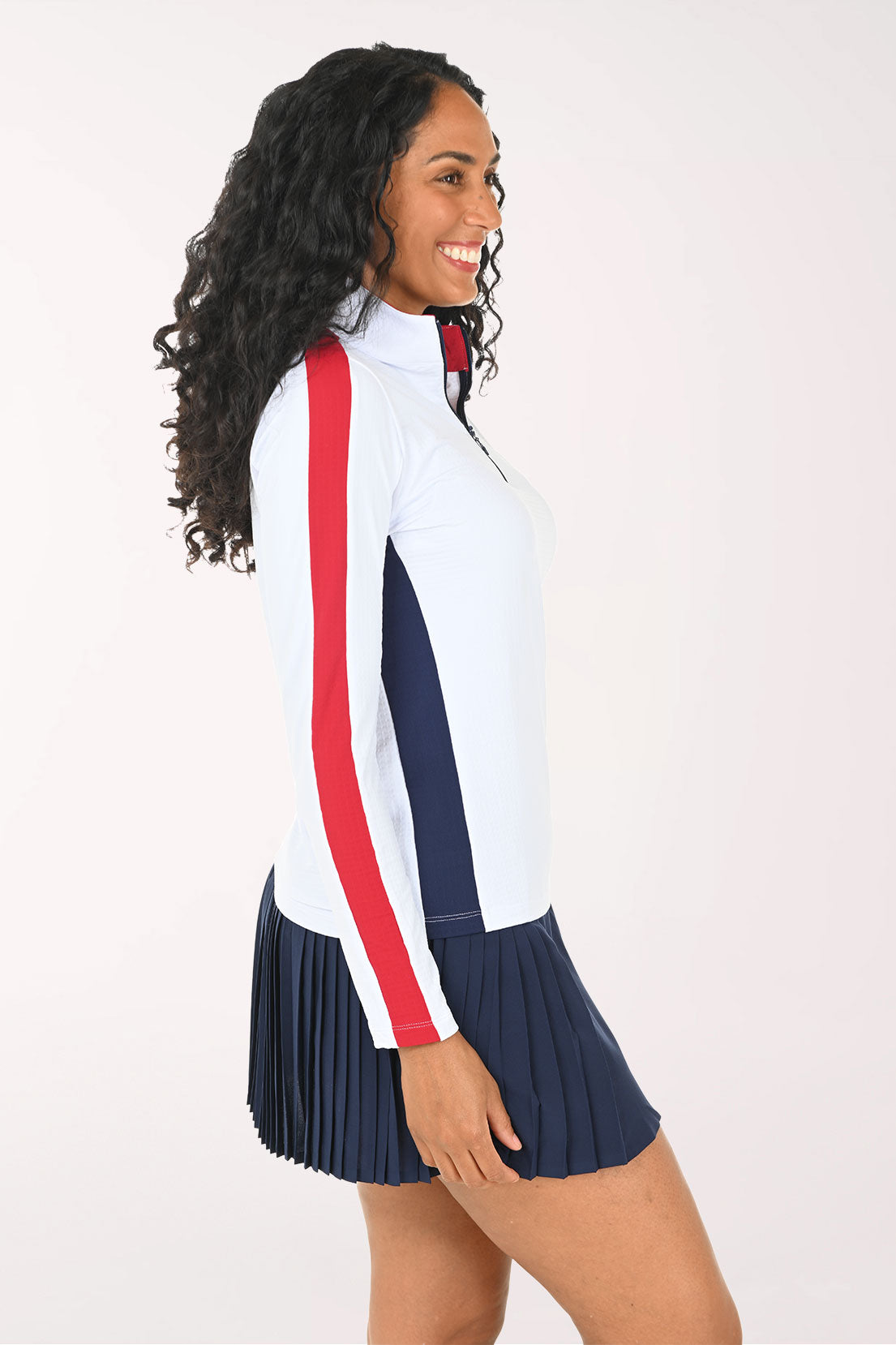 Woman wearing a white athletic top with red accents and a navy skirt on a white background