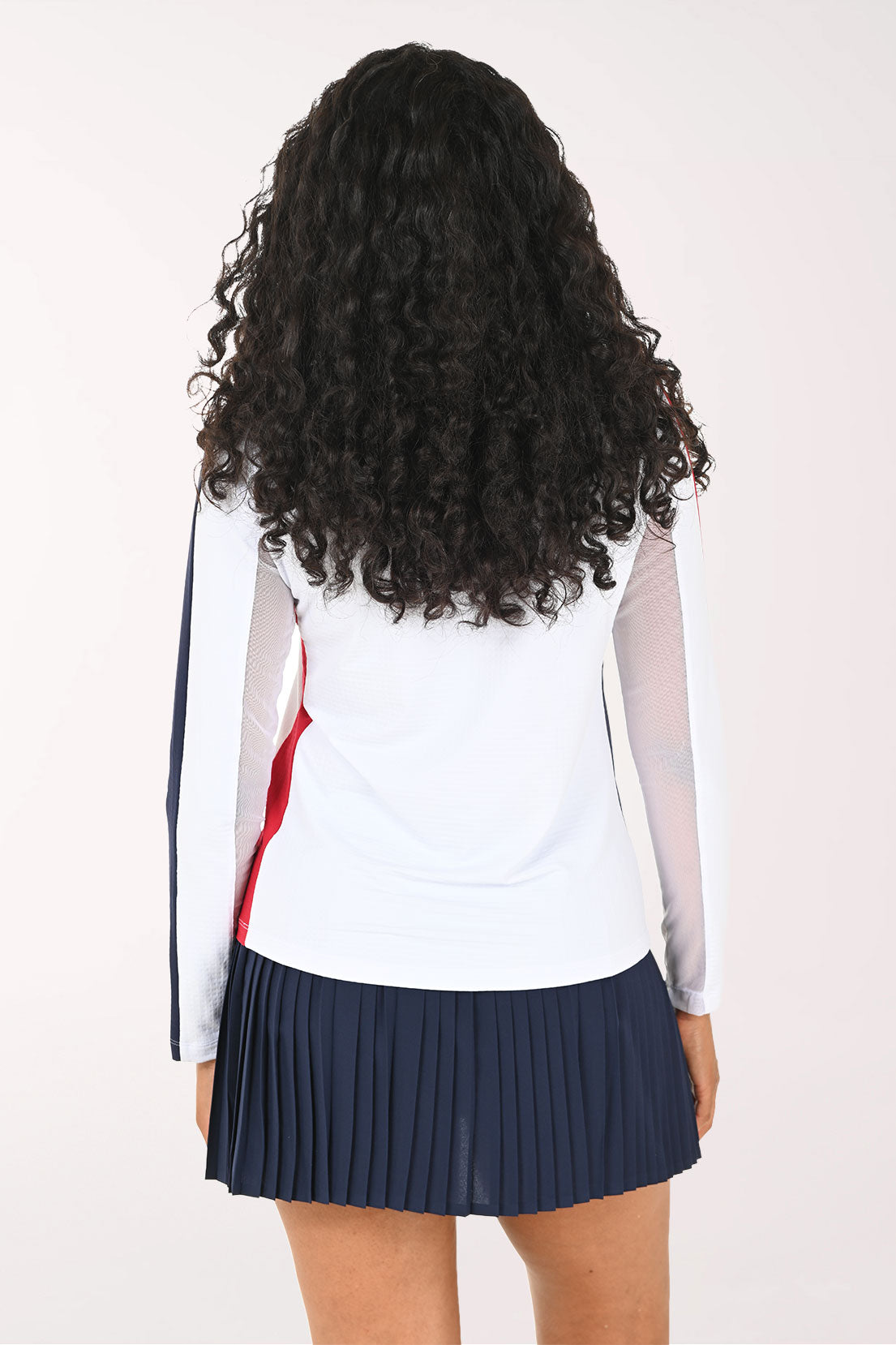Woman wearing a white athletic top with red accents and a navy skirt on a white background