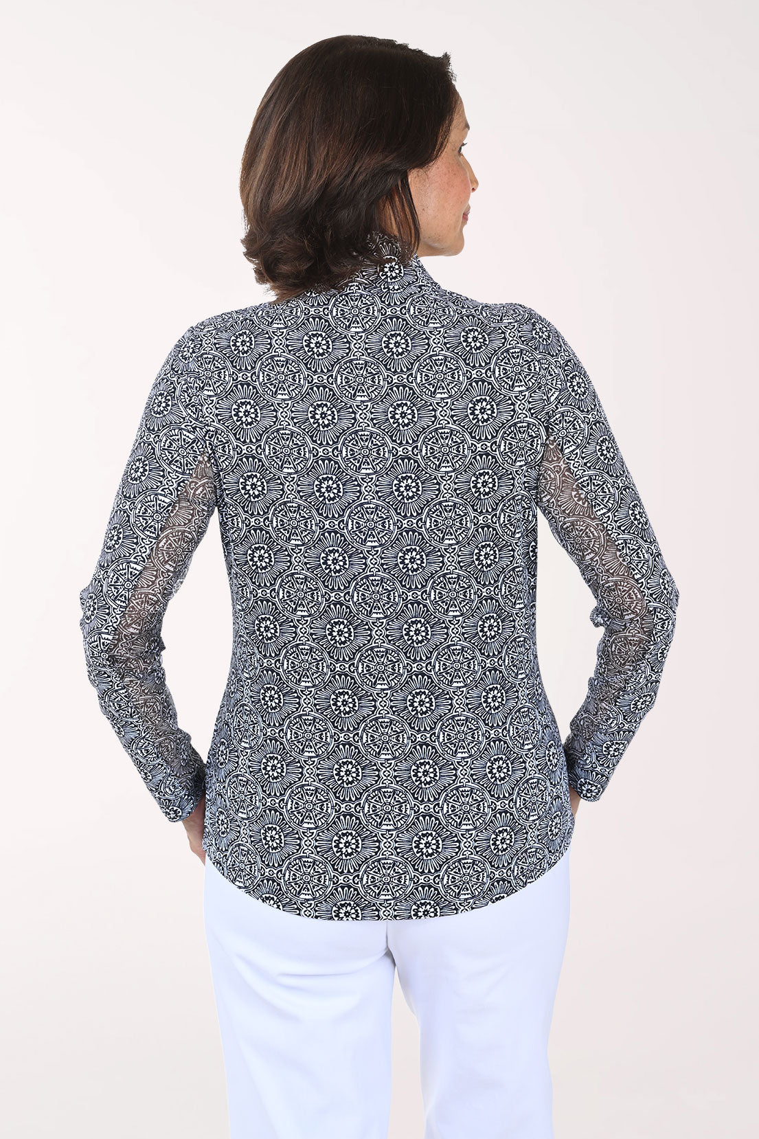 Woman wearing a patterned long-sleeve shirt and white pants on a plain background