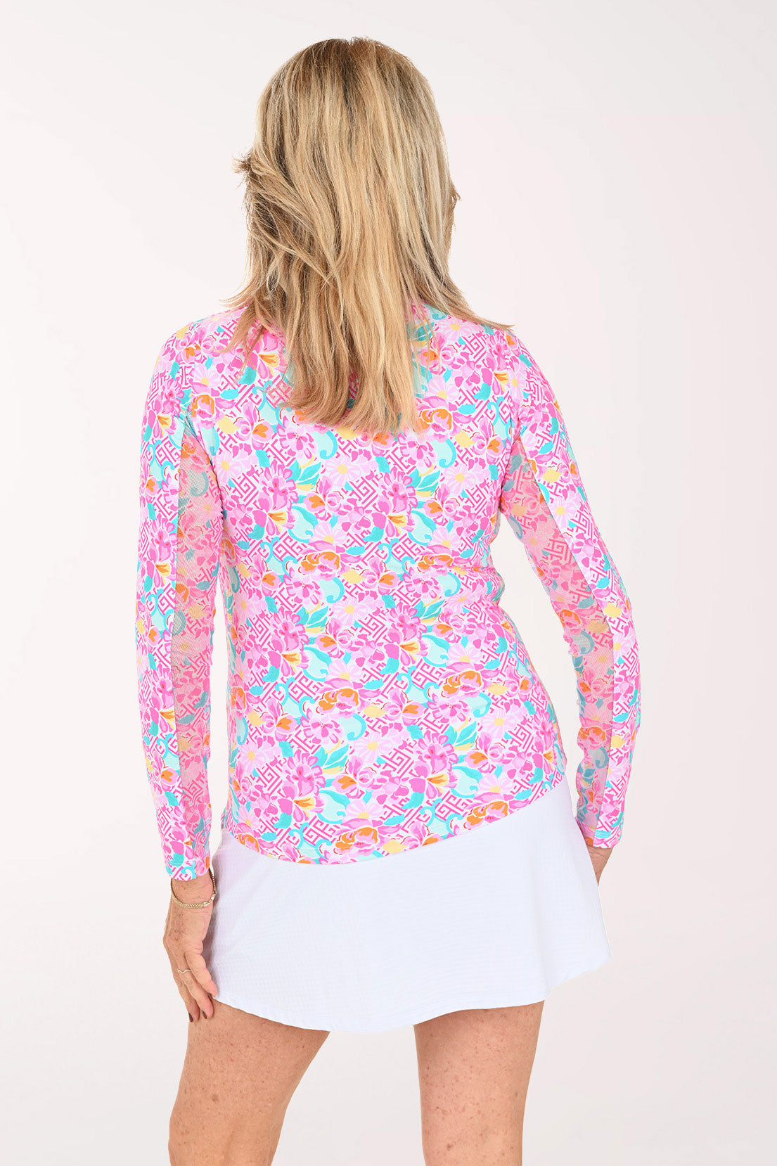 A woman modeling a long-sleeve collared top with a vibrant pink, blue, and orange floral pattern, paired with a white skirt, against a plain white studio background.