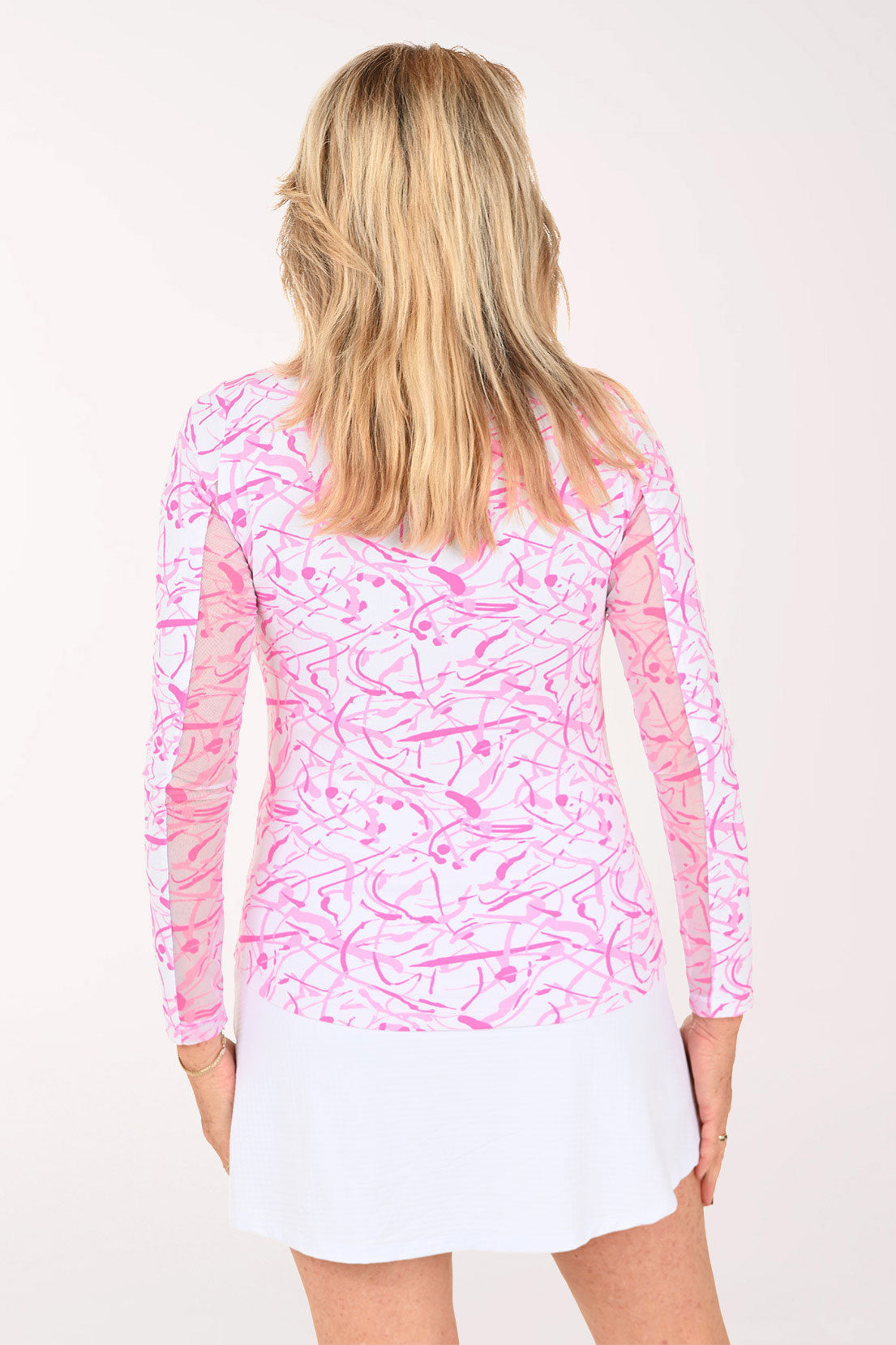A woman modeling a pink and white abstract patterned long-sleeve collared top with a white skirt, shown from a back profile against a plain white studio background.