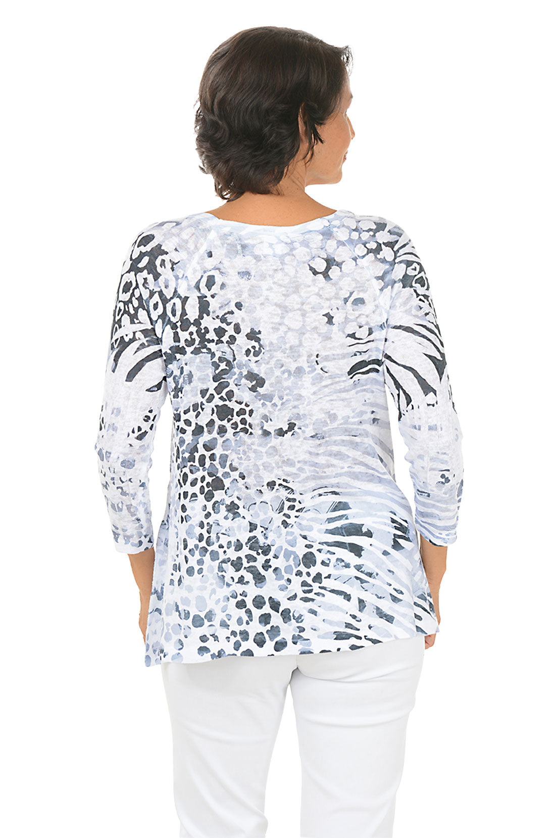 Woman wearing a patterned long-sleeve top and white pants on a white background. Back shot.