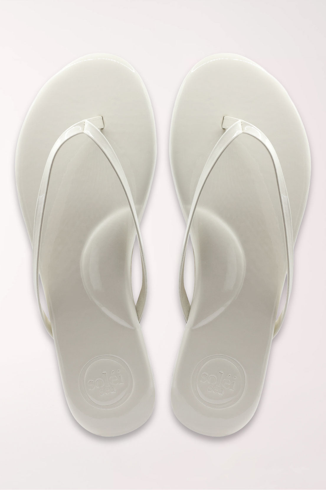 White flip-flop sandal with brown sole on a beige surface