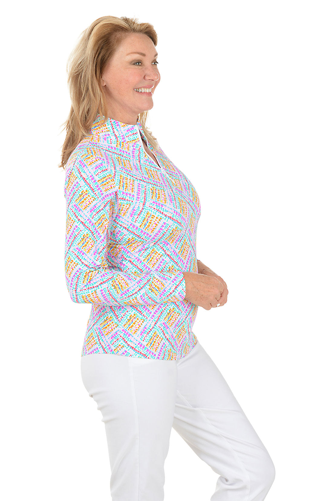 Woman wearing a colorful patterned blouse with white pants on a white background. Side shot.