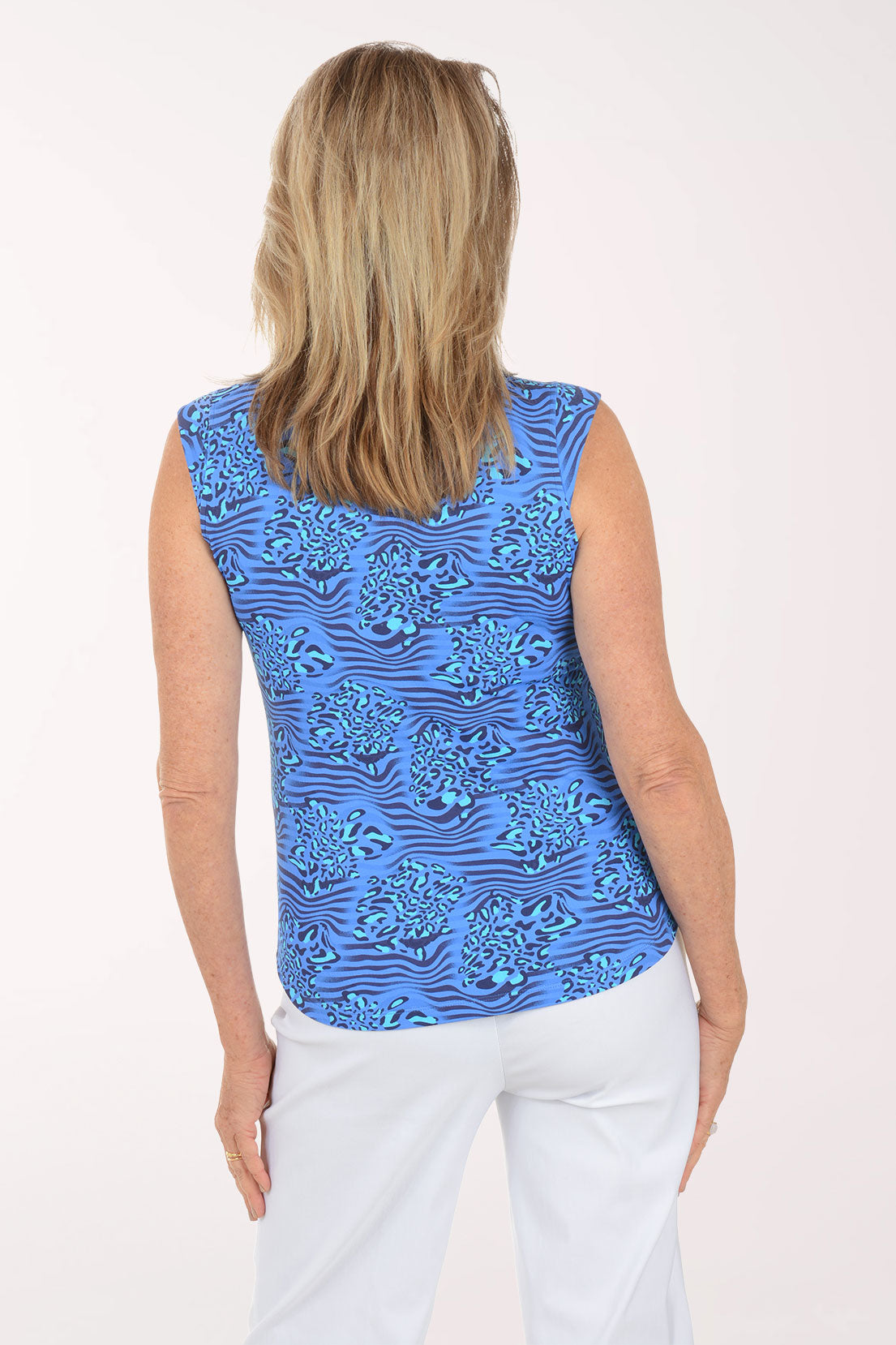 Woman wearing a blue patterned sleeveless top and white pants on a white background