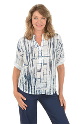 A woman wearing a white and navy 3/4 rolled sleeve top with a button detail and abstract pattern.