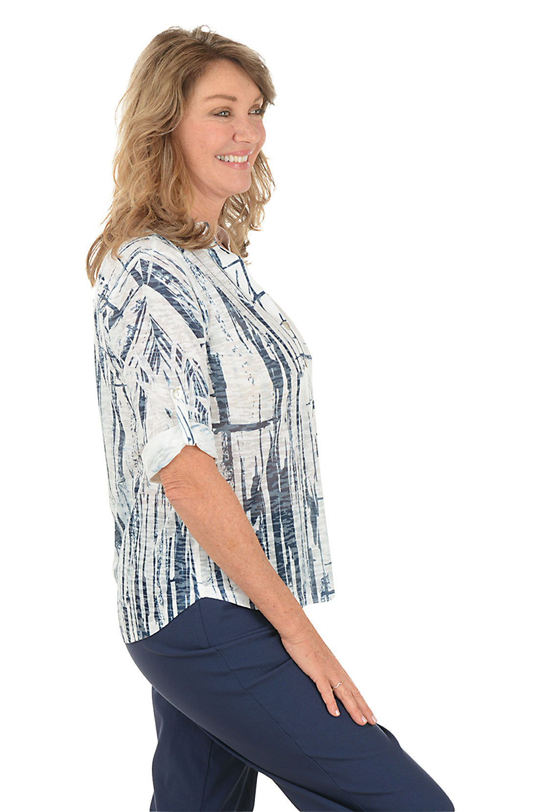 A woman wearing a white and navy 3/4 rolled sleeve top with a button detail and abstract pattern. Side shot.