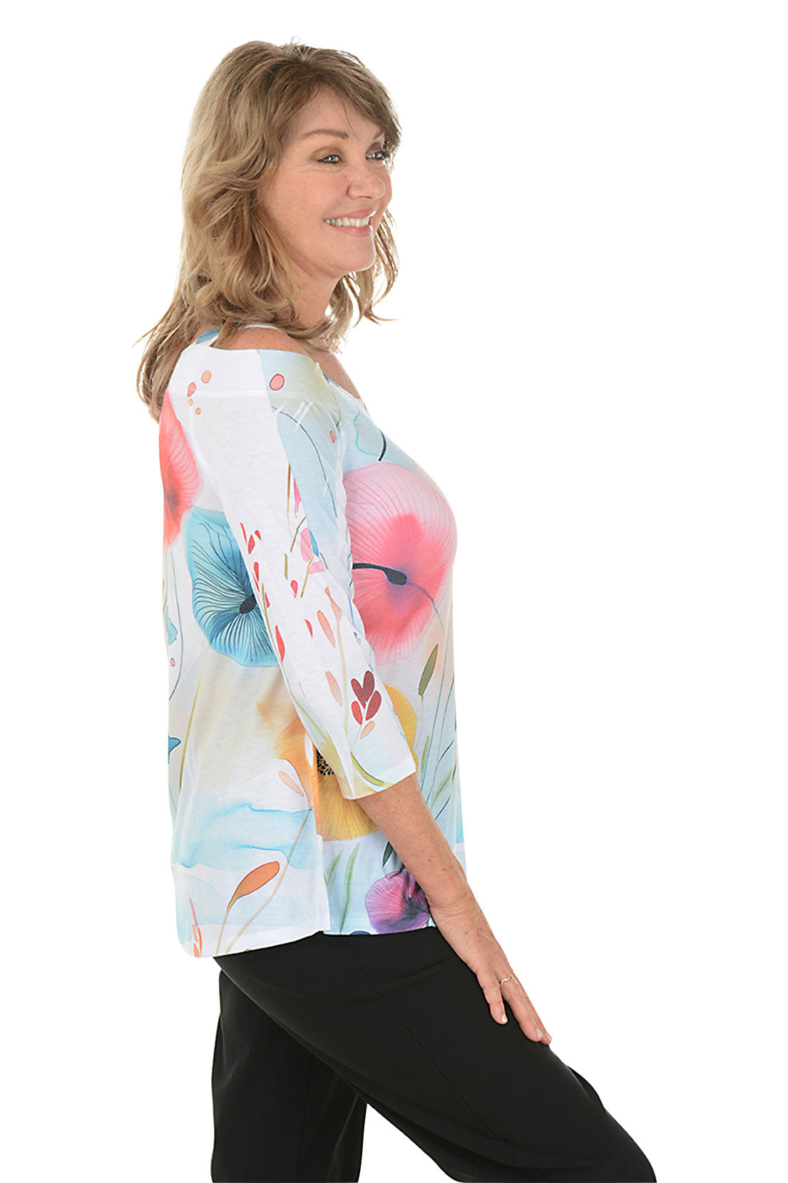 A woman wearing a 3/4 sleeve cold shoulder top in white with a multicolored watercolor floral print. Side shot.