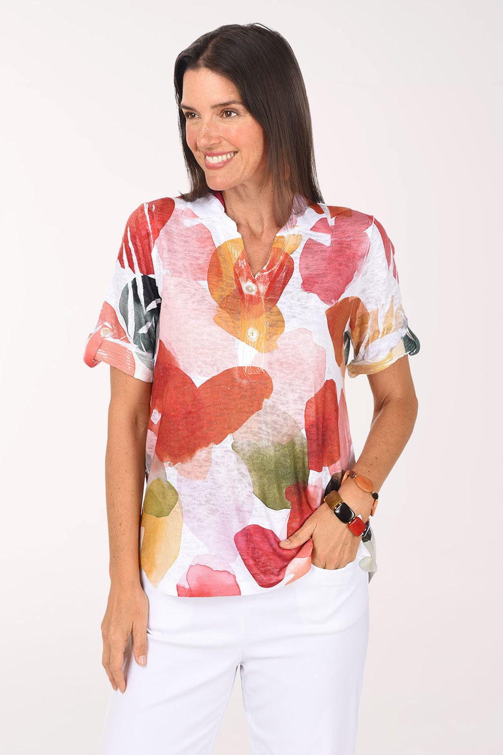 Model wearing the Impulse Drifting Petals Sequin Accented Polo Top, white with oversized red, coral and golden yellow petals, over white pants, front view