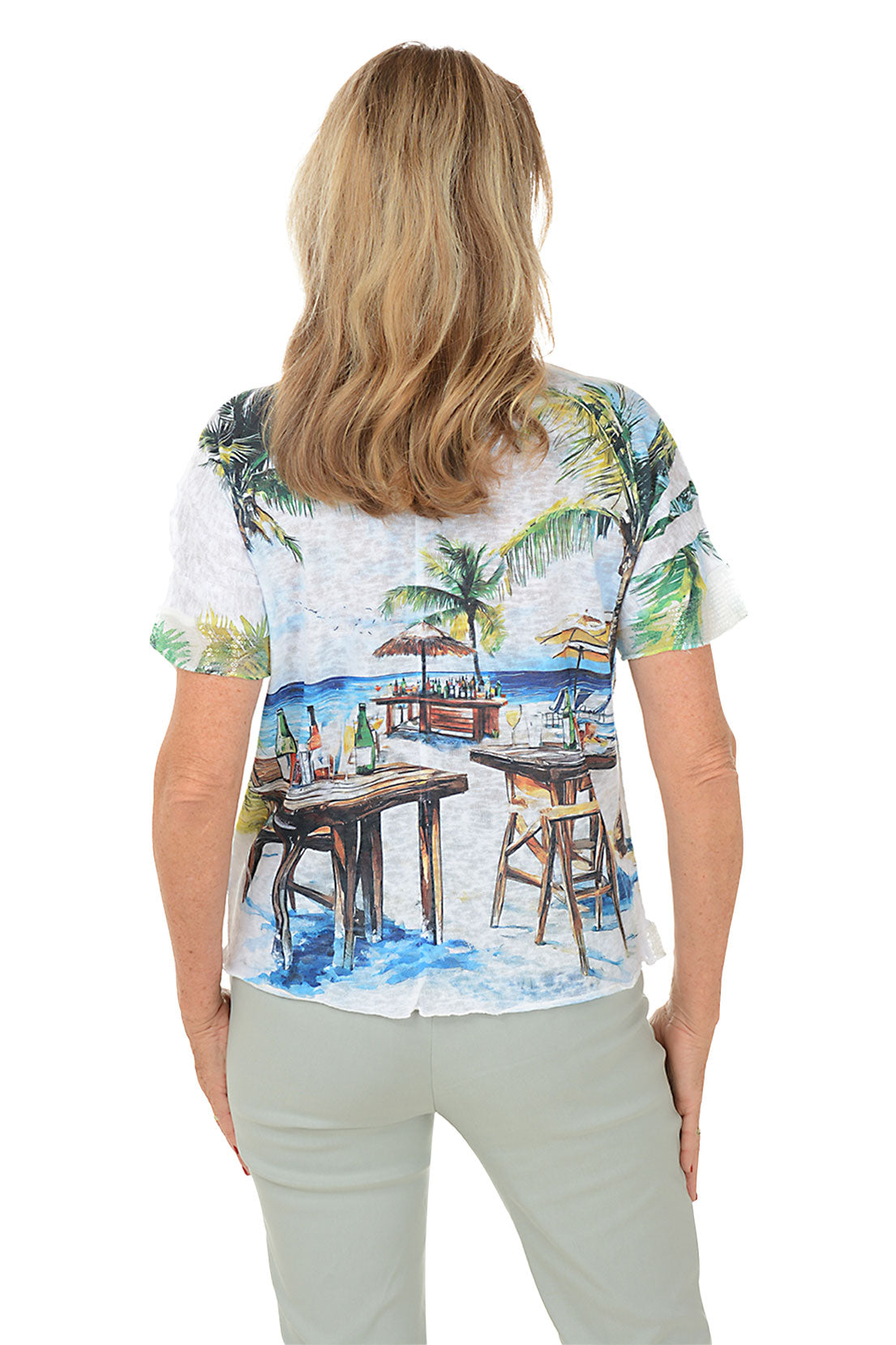 A back shot of a model wearing a white scoop neck knit top with short dolman sleeves and sequined cuffs, featuring a beach bar print.
