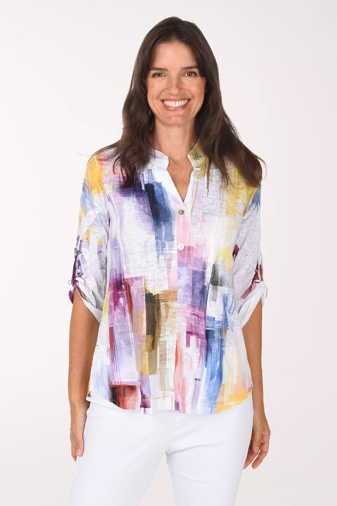 Smiling woman in a white roll sleeve top with a watercolor brushstroke print in violet, pink, saffron and sky blue, a sequined mandarin collar and split V-neck placket, worn with white pants