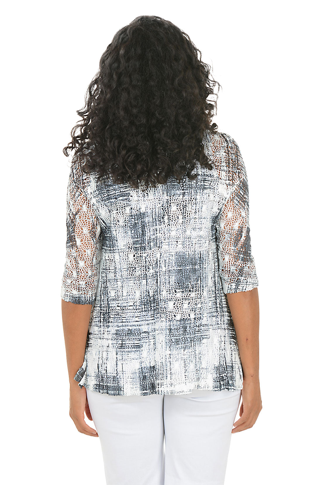 Woman wearing a patterned top with matching sweater and white pants on a white background. Back shot.