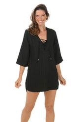A front shot of a model wearing a black 3/4 sleeve tunic cover-up with lace-up v-neckline and dual hip pockets.