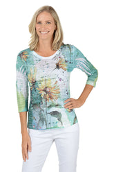 A woman wearing a 3/4 sleeve multicolored top with a sunflower pattern.