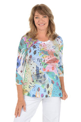 A woman wearing a 3/4 sleeve multicolored top with an abstract pattern.