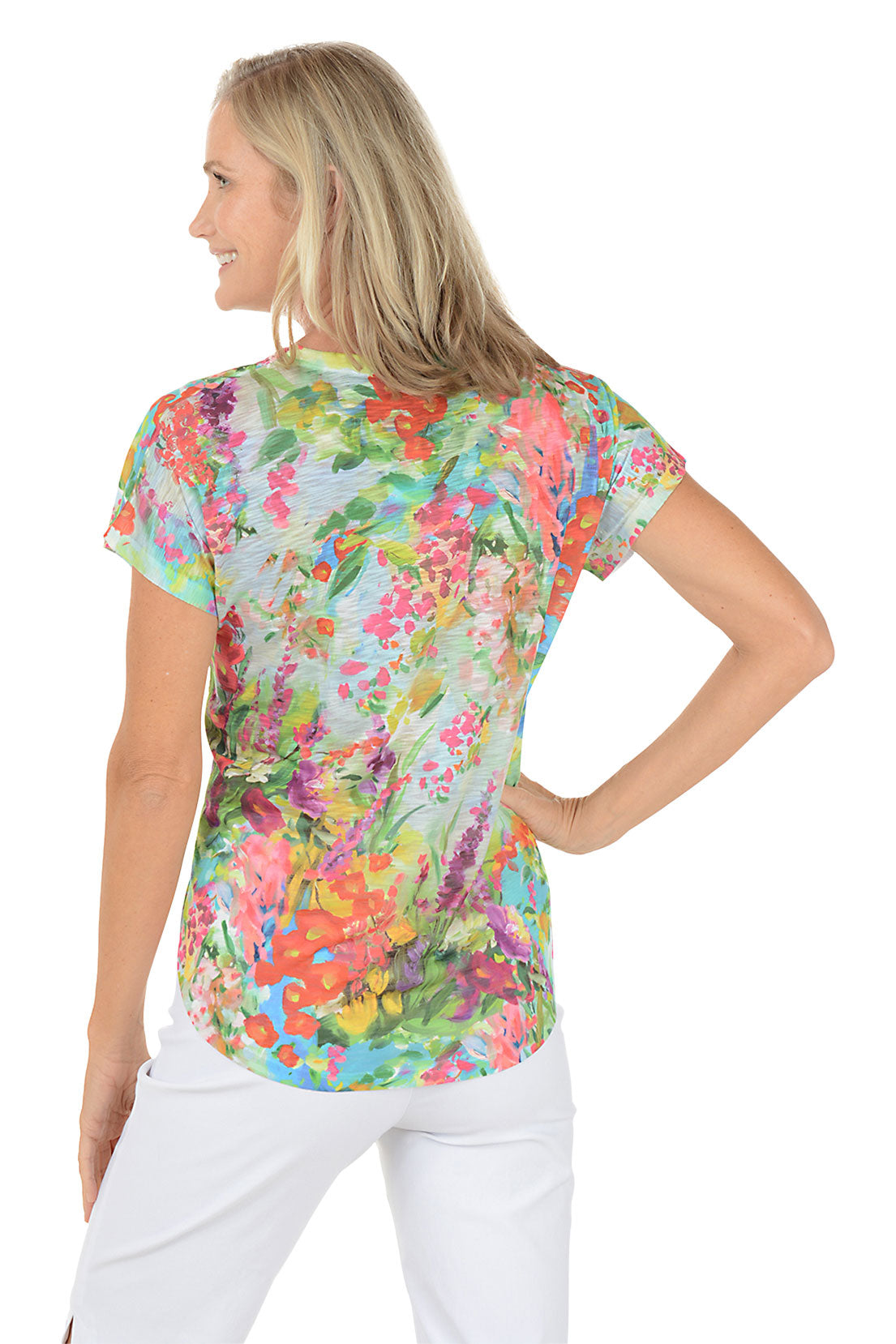 Woman wearing a colorful floral blouse with white pants on a white background. Back shot.